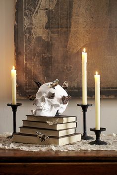 a skull sitting on top of some books with candles in front of it and a painting behind it