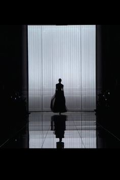 a black and white photo of a person in a dark room with curtains behind them