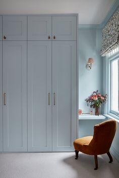 an orange chair sits in front of a white closet with many doors and drawers on the wall