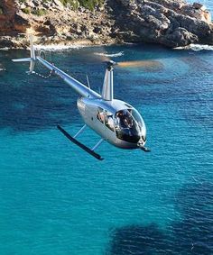 a small plane flying over the ocean next to a rocky cliff and shore line with clear blue water