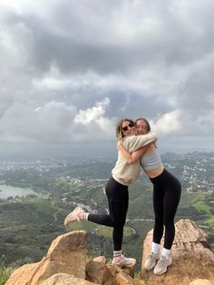 two women hugging each other on top of a mountain