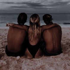 three people sitting on the beach looking out at the ocean