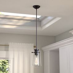 a light fixture hanging from the ceiling in a kitchen with white cabinets and windows behind it