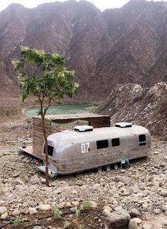 an old camper sits in the middle of a rocky area with mountains in the background