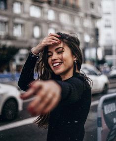 a woman smiles as she walks down the street with her hand in front of her face