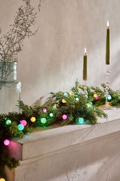 a mantle with candles and garland on it next to a vase filled with greenery