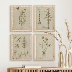 three framed pictures on the wall above a wooden table with vases and plants in it