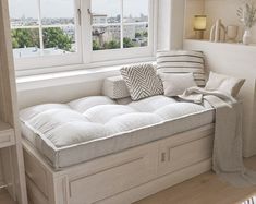 a white day bed with pillows on it in front of a window overlooking the city