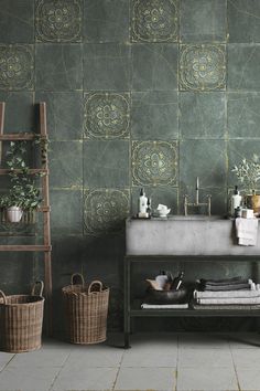 a bathroom with green tiled walls and flooring next to a wooden shelf filled with towels