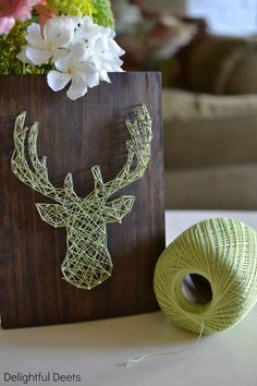 a string art deer head on a wood block next to a ball of green yarn