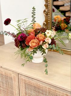 a vase filled with flowers sitting on top of a wooden dresser next to a mirror