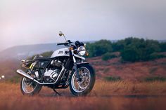 a motorcycle parked on the side of a dirt road in front of some grass and trees