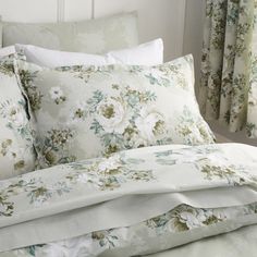 a bed with white and green floral comforter on it's side, next to a window