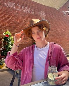 a young man wearing a cowboy hat and holding a drink in front of his face