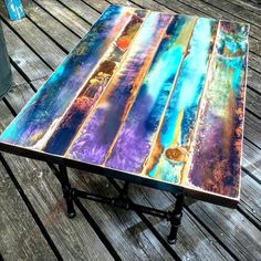 a table made out of old wood with colorful paint on the top and bottom, sitting on a wooden deck