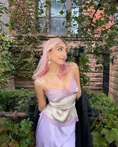 a woman with pink hair wearing a purple and silver dress in front of a house