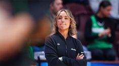 a women's basketball coach watches her team during a game with other players in the background