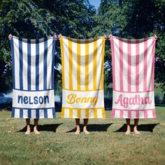 three people standing in the grass holding up towels with name on them and two are wearing sandals