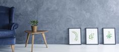 a blue chair sitting next to two framed pictures and a plant in a vase on a table