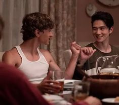 two young men sitting at a table with food and drinks in front of their faces