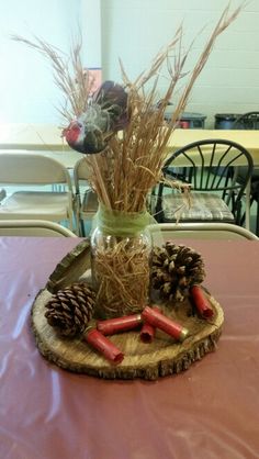 a vase filled with flowers and pine cones on top of a wooden tray covered in hay