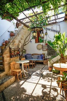 an outdoor seating area with tables and chairs under a trellis covered roof, surrounded by greenery