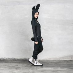 a woman in a black bunny suit and white converses is standing against a wall