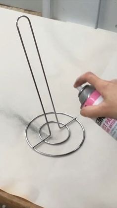 a person is spray painting on a piece of white paper with silver paint and a metal holder