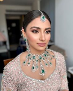 a woman wearing an elaborate necklace and earrings with green jewels on her neck, standing in front of a table