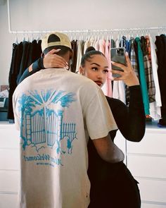 a man and woman standing in front of a rack of shirts