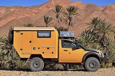 a yellow truck parked in the desert with palm trees and mountains in the back ground