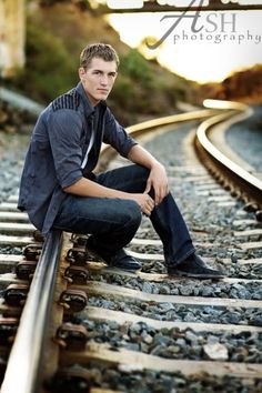 a young man is sitting on the railroad tracks and posing for a photo with his hands in his pockets