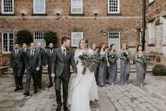 a bride and groom walking with their bridal party in front of a brick building