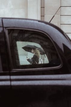 a woman holding an umbrella is reflected in the rear view mirror of a black car