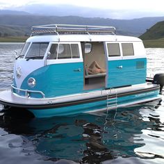 a blue and white vw bus floating on top of the water next to mountains