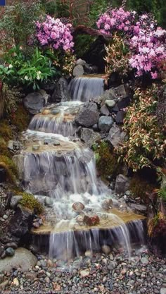 a small waterfall surrounded by rocks and flowers