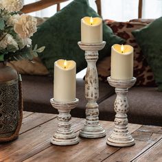 three white candles sitting on top of a wooden table next to a vase filled with flowers