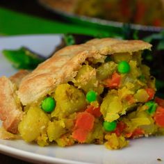 a piece of vegetable pie on a plate with peas and carrots in the background