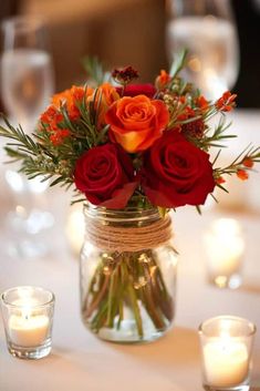 a vase filled with red and orange flowers on top of a table next to candles