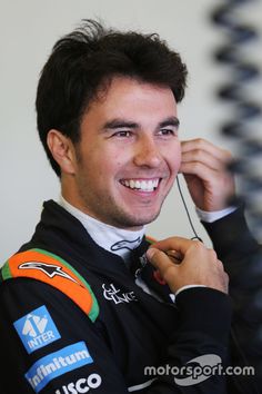 a man in a racing suit smiling and adjusting his earpieces on the side of his head