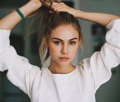 a young woman is holding her hair in one hand and looking at the camera while wearing a white top