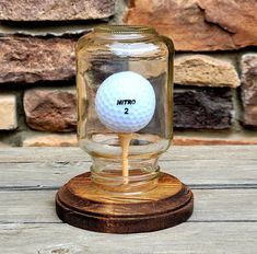 a glass jar with a golf ball in it sitting on top of a wooden base