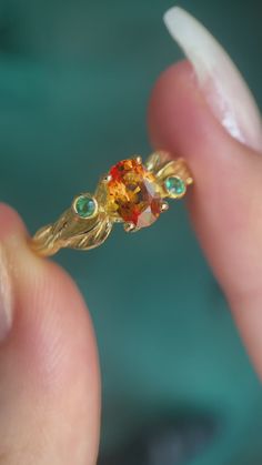 a close up of a person's hand holding a gold ring with colorful stones