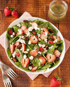 a salad with strawberries and feta cheese in a white bowl on a wooden table