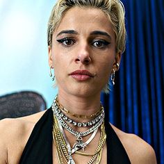 a woman in a black dress with multiple necklaces on her neck and one eye open