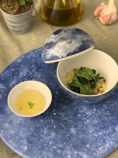 a blue plate topped with two white bowls filled with food next to a bottle of olive oil