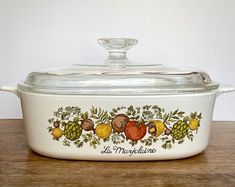 a casserole dish with fruit and vegetables painted on the side, sitting on a wooden table