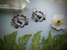 two pairs of earrings sitting on top of a table next to a white flower and green leaves