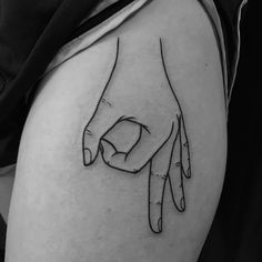 a black and white photo of a hand tattoo on the right thigh, which has two fingers pointing towards each other