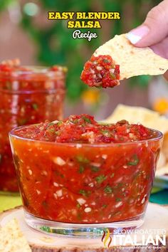 a person dipping salsa into a glass bowl with tortilla chips on the side